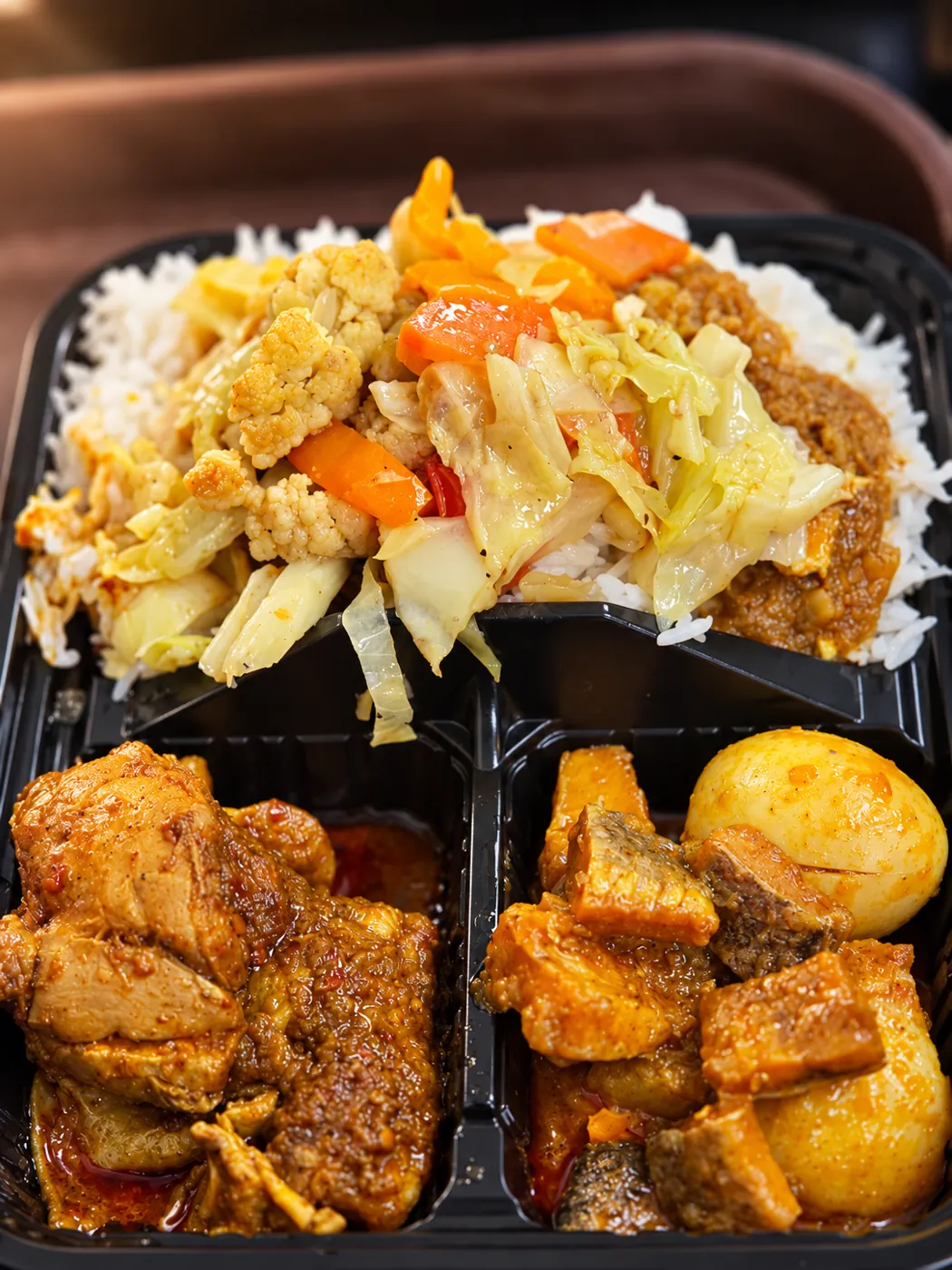 Takeaway tray of rice with curries, stir-fried vegetables and a boiled egg