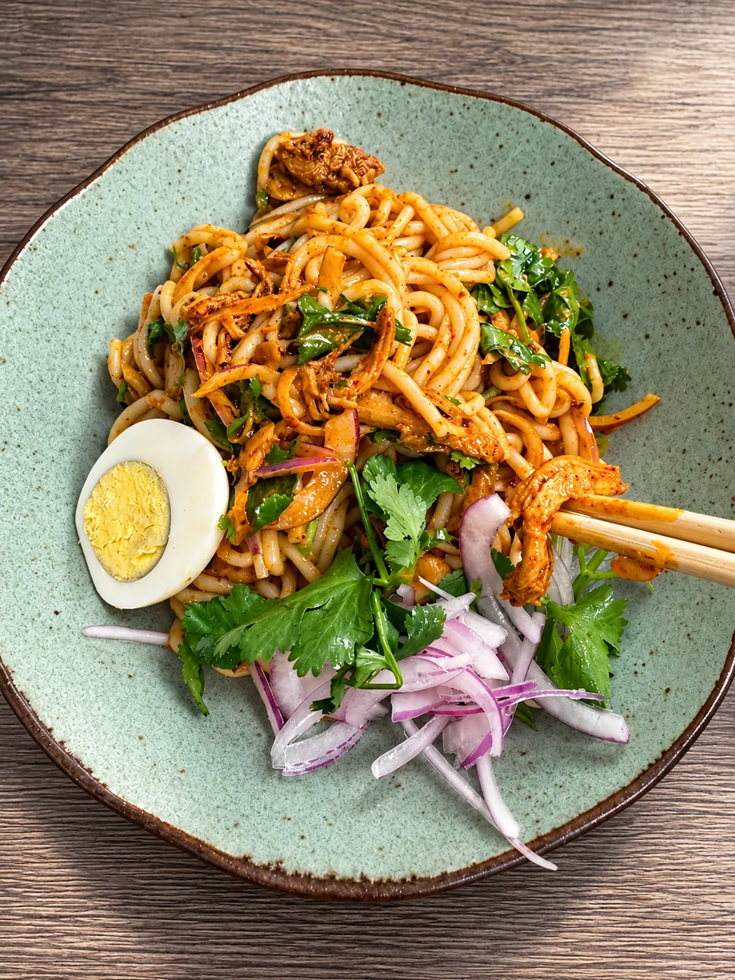 Noodle salad with shredded chicken, cilantro, red onion and a halved boiled egg