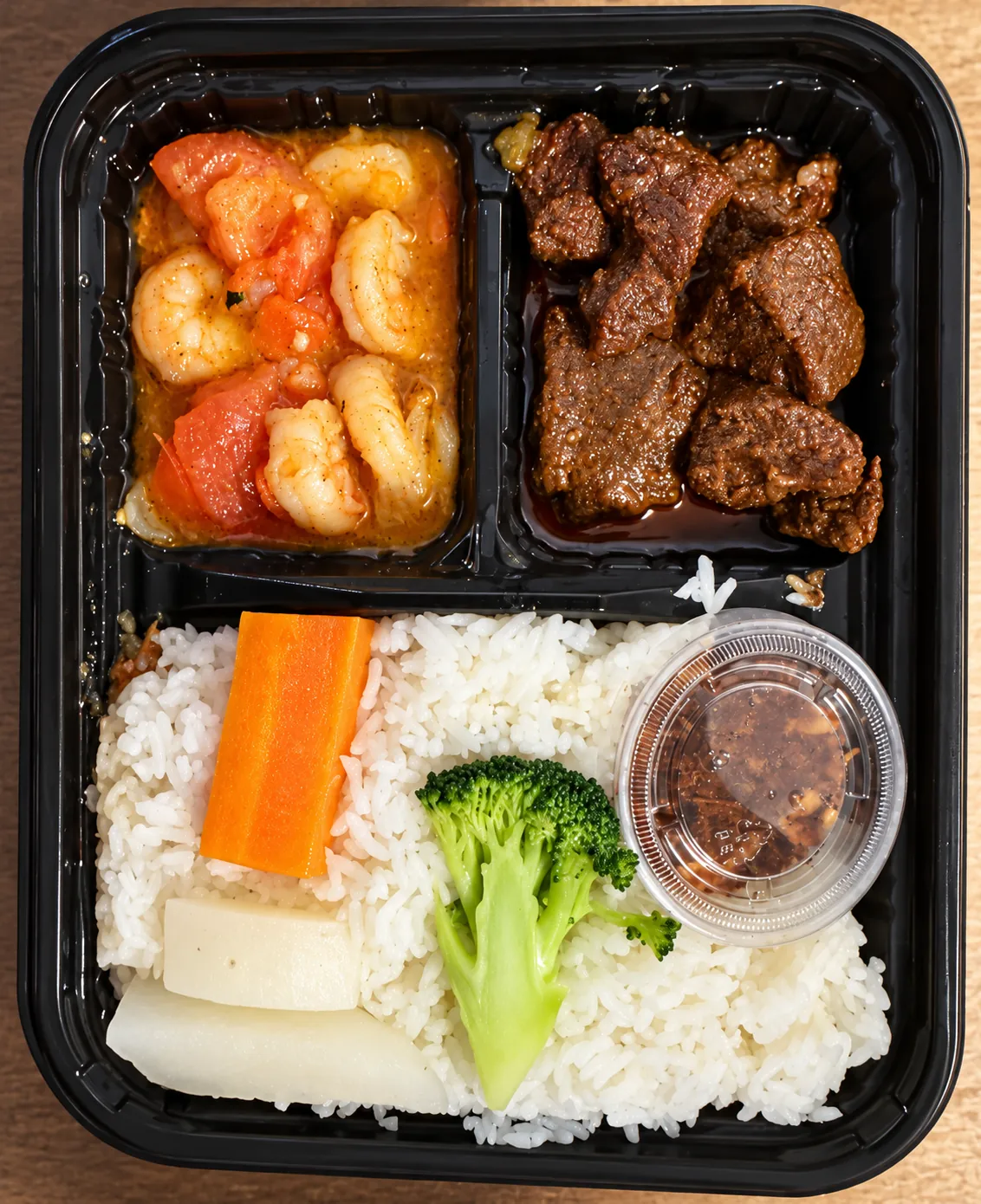 Takeaway tray with shrimp in tomato sauce, braised meat, rice, carrot, broccoli and a sauce cup